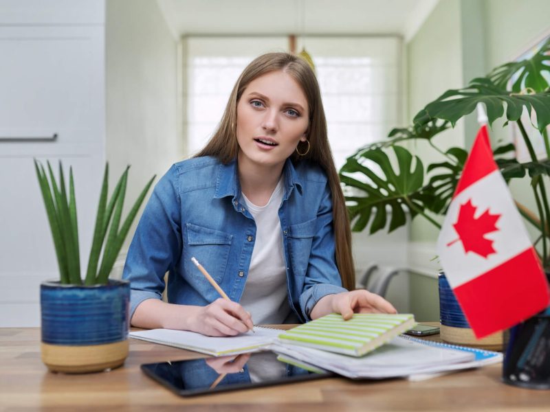 online-training-female-teenager-sitting-at-home-looking-at-webcam-canadian-flag-on-table.jpg